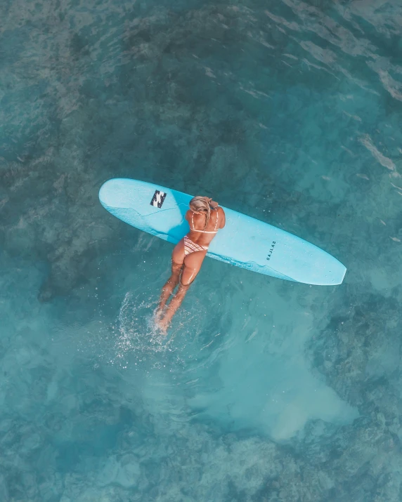 a woman that is standing in the water with a surfboard, from above, light blue skin, thumbnail, tans