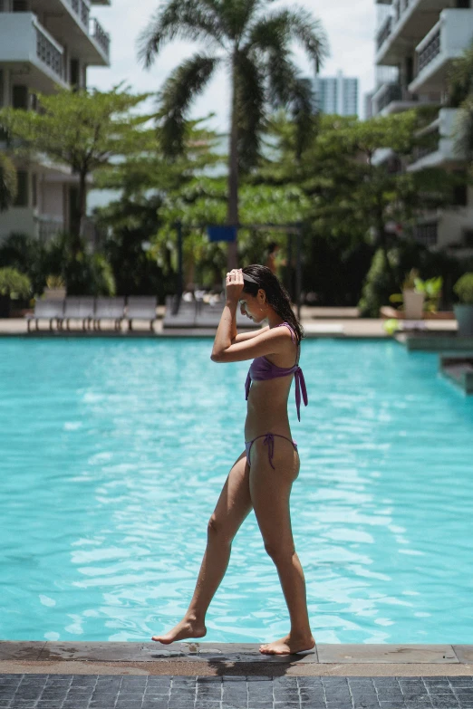 a woman in a bikini standing in front of a swimming pool, walking away from the camera, bangkok, purple, doing a sassy pose
