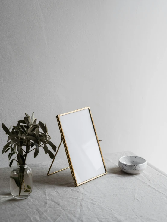 a picture frame sitting on top of a table next to a plant, by Rebecca Horn, brass plated, high quality product photo, scandinavian, folded