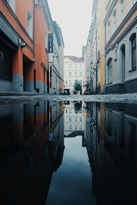 a reflection of buildings in a puddle of water, unsplash contest winner, gray and orange colours, old town, after rain, square