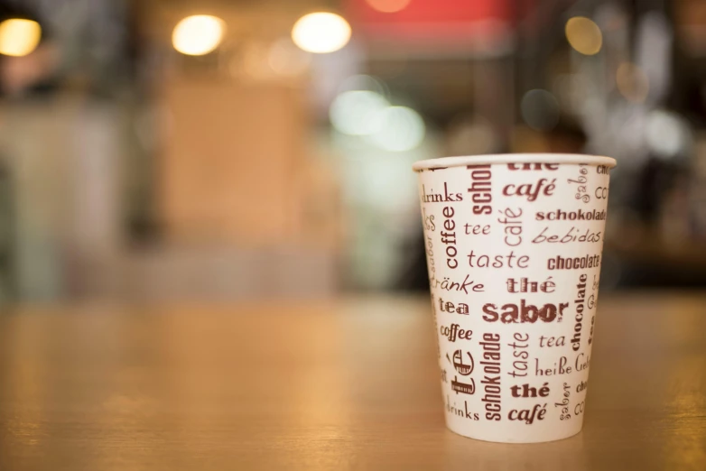 a coffee cup sitting on top of a wooden table, graffiti, sabbas, background image, at the counter, strong bespoke shape language