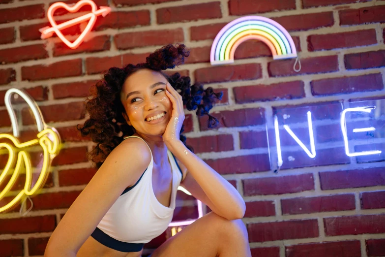 a woman posing in front of a brick wall with neon signs, trending on pexels, golden rainbow tubing, mixed race woman, bralette, teenager hangout spot