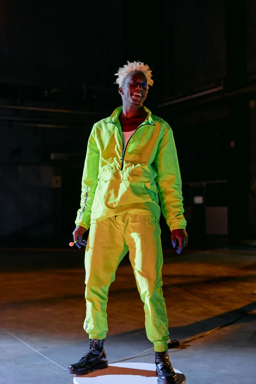 a man in a yellow suit standing on a skateboard, by Barthélemy Menn, trending on pexels, visual art, neon hair, dramatic green lighting, wearing a track suit, in an arena pit