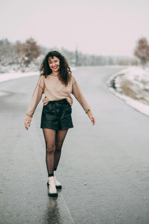 a woman walking down a road in the snow, an album cover, trending on pexels, renaissance, black leather shorts, satisfied pose, curly haired, tights