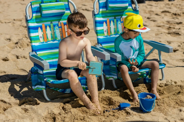 two young boys sitting in lawn chairs on the beach, green and blue and warm theme, crowded beach, striped, 3 - piece