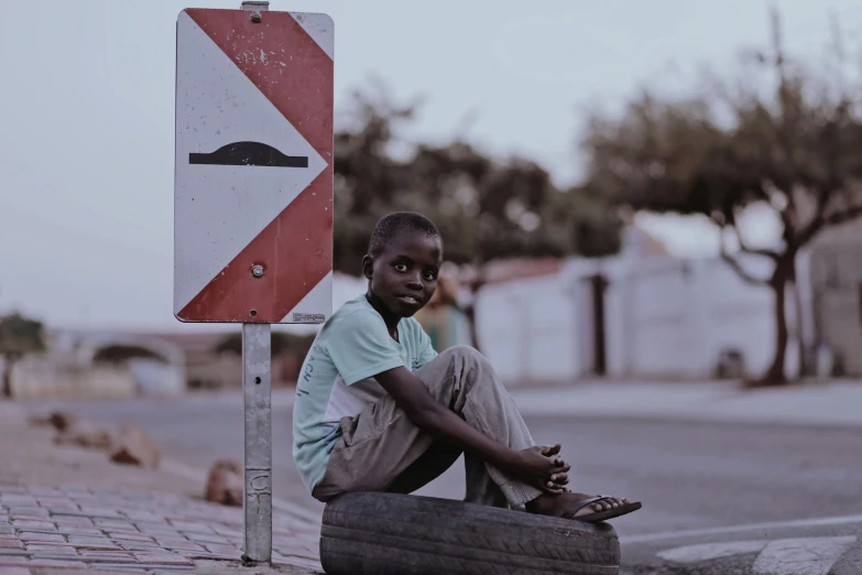 a young boy sitting on the ground next to a street sign, pexels contest winner, happening, in africa, high detailed photo, ignant, a small