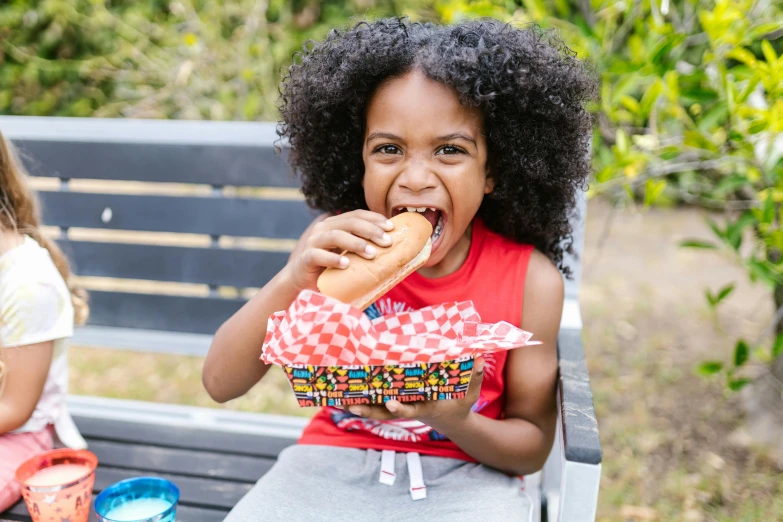 a little girl sitting on a bench eating a hot dog, pexels contest winner, nerdy black girl super hero, patterned, picnic, modelling