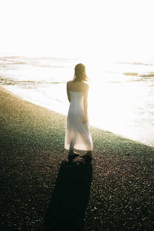 a woman in a white dress standing on a beach, inspired by Elsa Bleda, unsplash, back lit, medium format. soft light, sun - drenched, iceland