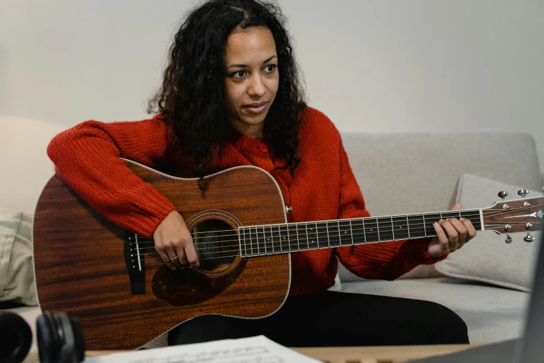 a woman sitting on a couch playing a guitar, inspired by Ella Guru, hurufiyya, sydney park, looking across the shoulder, student, holding guitars