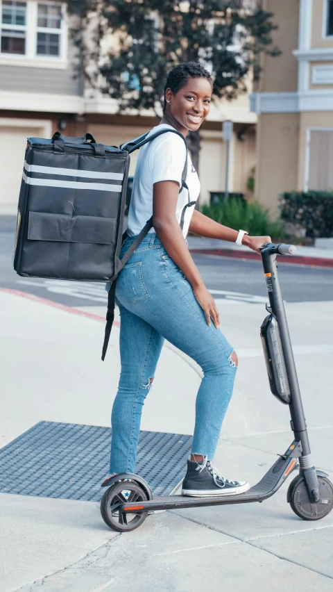 a woman riding a scooter on a city street, trending on pexels, happening, square backpack, maria borges, back and standing, los angeles ca