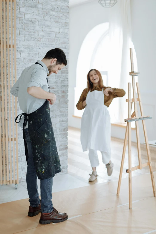 a man standing next to a woman in a room, a painting, inspired by artist, pexels contest winner, wearing an apron, having fun, white studio, 15081959 21121991 01012000 4k