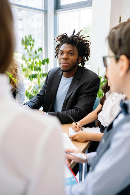 a group of people sitting around a wooden table, black man with afro hair, in a meeting room, professional grade, lgbtq