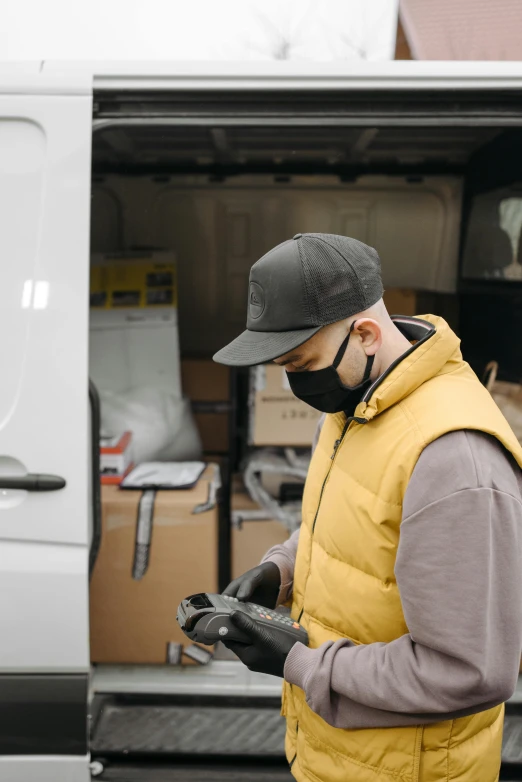 a man wearing a face mask standing in front of a van, pexels, scanning items with smartphone, yellow overall, wide screenshot, grey