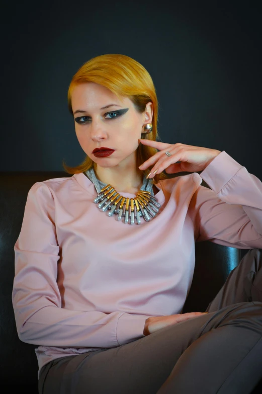 a woman sitting on a couch talking on a cell phone, a portrait, inspired by Vasile Hutopila, pixabay contest winner, wearing gold detailed choker, egypt makeup, pink and grey muted colors, wearing steel collar