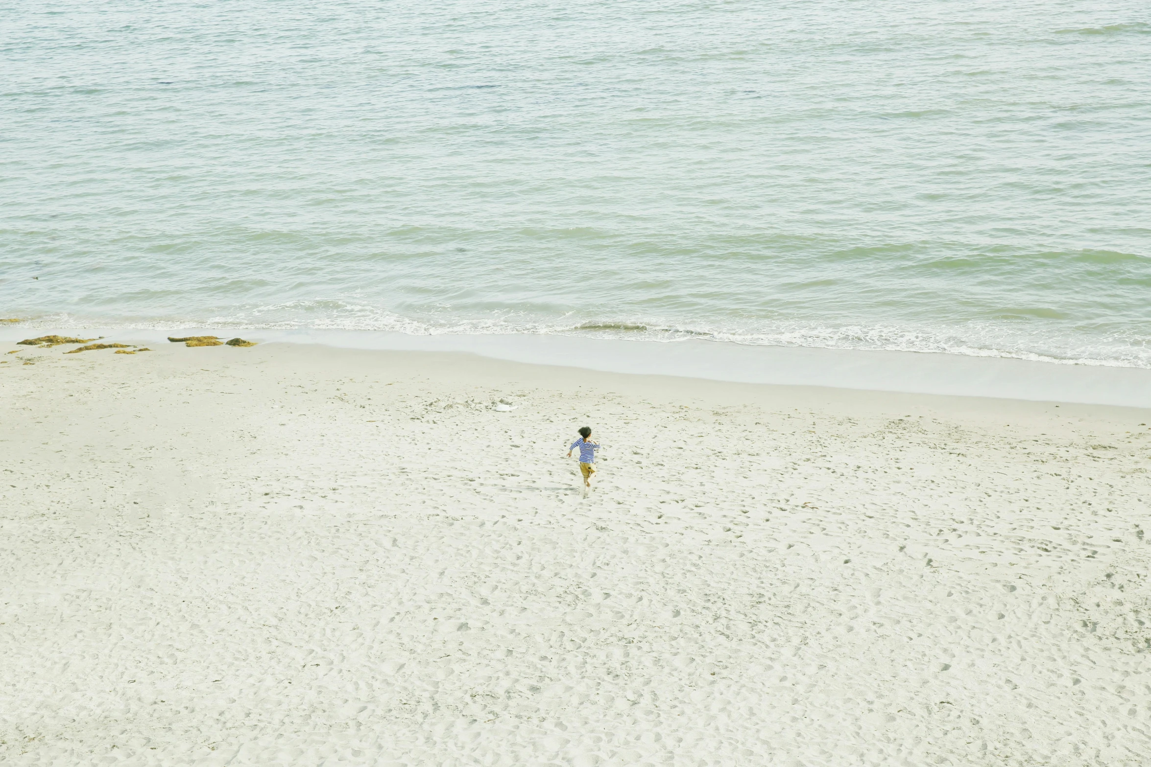 a person standing on a beach next to the ocean, from a distance, little kid, ignant, wide overhead shot