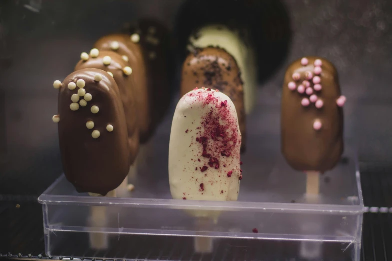 a display of chocolate covered pops with sprinkles, by Lee Loughridge, unsplash, art nouveau, eating ice - cream, white with chocolate brown spots, manuka, close - up photo