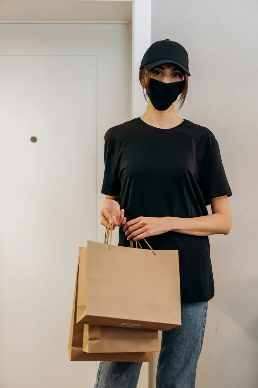 a woman wearing a face mask holding shopping bags, he is wearing a black t-shirt, brown paper, dark visor covering eyes, asian face