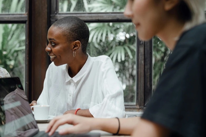 two women sitting at a table with a laptop, pexels contest winner, happening, black female, background image, in meeting together, low quality photo