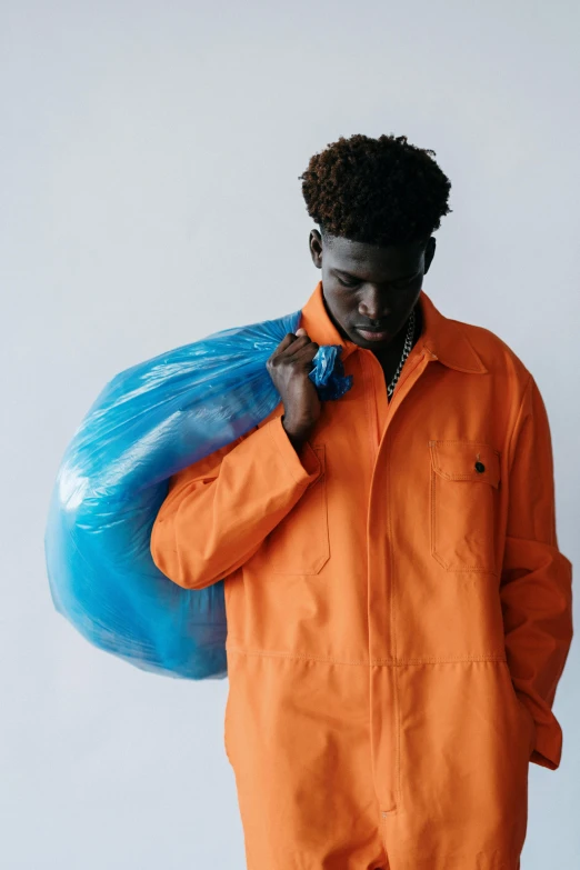 a man in an orange coverall holding a blue bag, pexels contest winner, arte povera, adut akech, wearing a plastic garbage bag, promotional image, profile pic