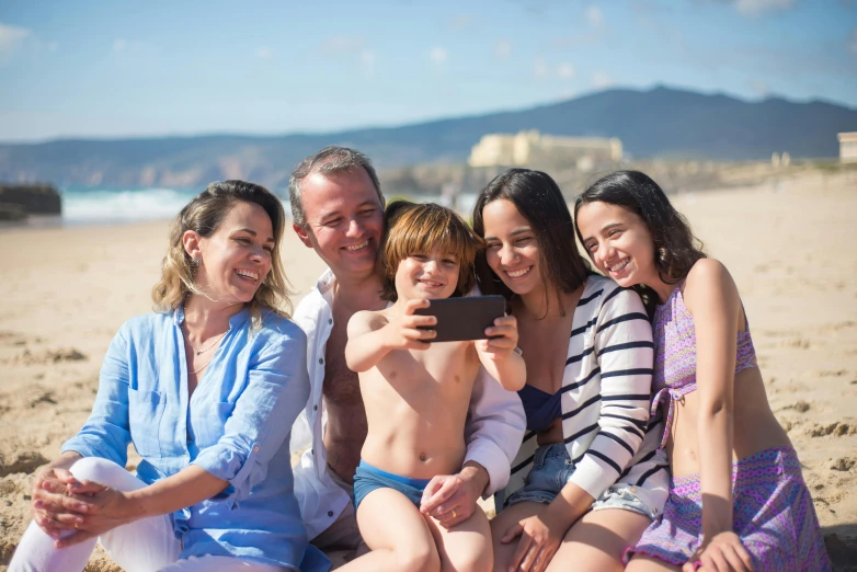 a group of people sitting on top of a sandy beach, a picture, taking a selfie, families playing, avatar image, spanish