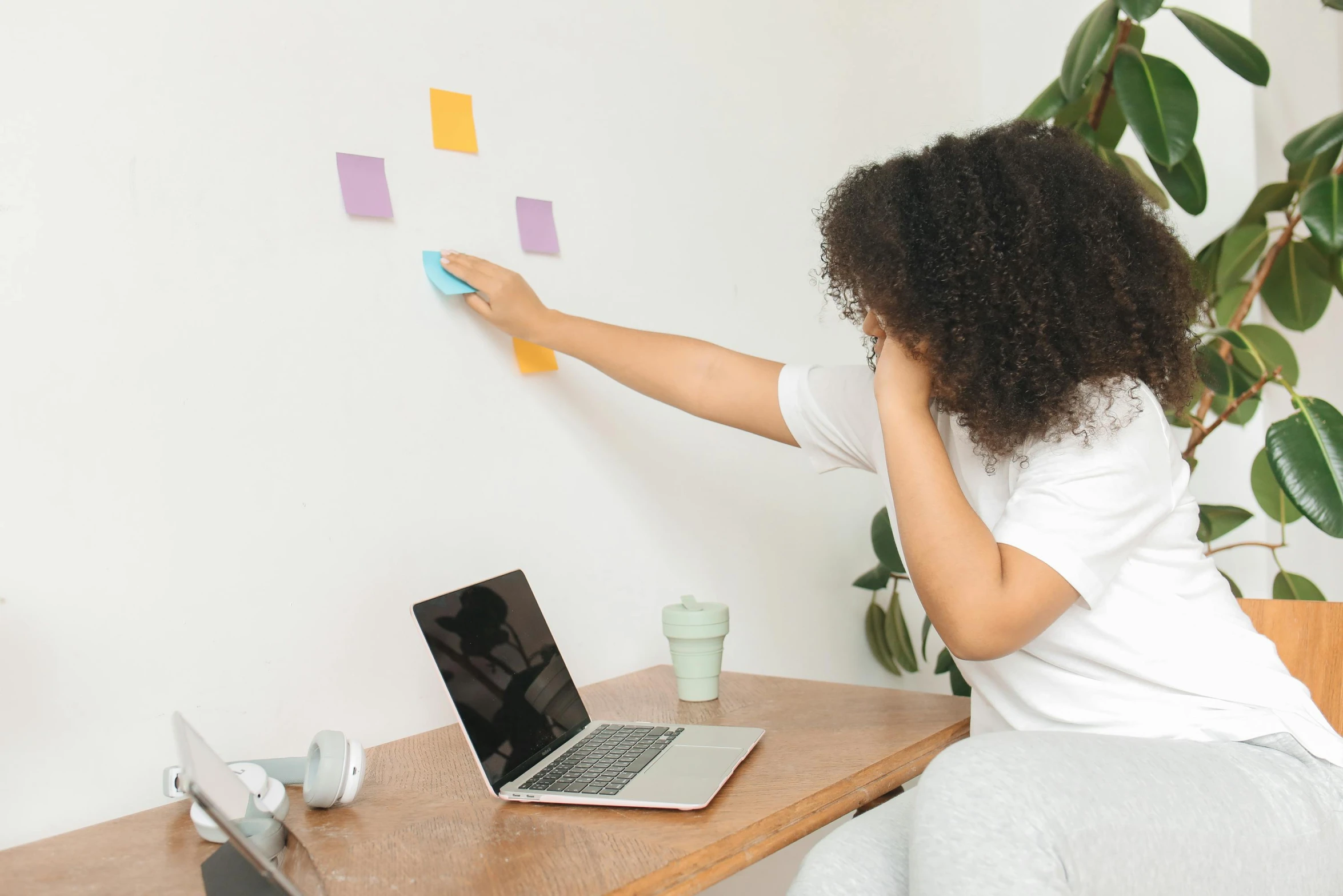 a woman sitting at a desk with a laptop and sticky notes on the wall, trending on pexels, interactive art, square sticker, pointing, afro tech, tiny room with dirty wall tiles