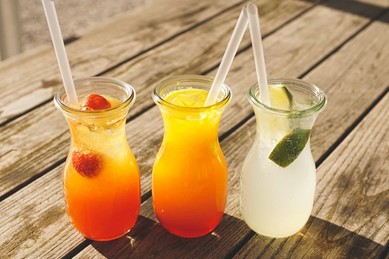 a couple of drinks sitting on top of a wooden table, fruit, 3 colours, with a straw, 6 pack