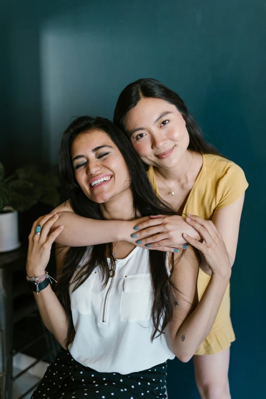 a couple of women standing next to each other, trending on pexels, dau-al-set, olive skin color, at home, woman with black hair, embrace