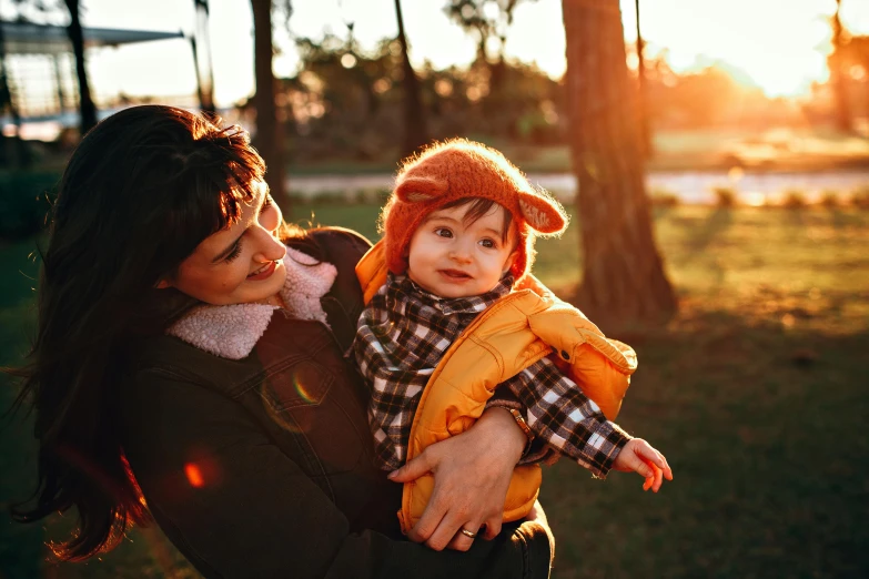 a woman holding a baby in her arms, by Julia Pishtar, pexels, golden sunlight, square, beanie, little boy