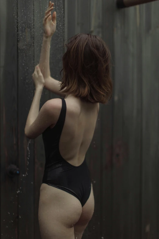 a woman in a bathing suit leaning against a fence, inspired by Elsa Bleda, unsplash, renaissance, dark black porcelain skin, back - view, karen gillan, muted colored bodysuit