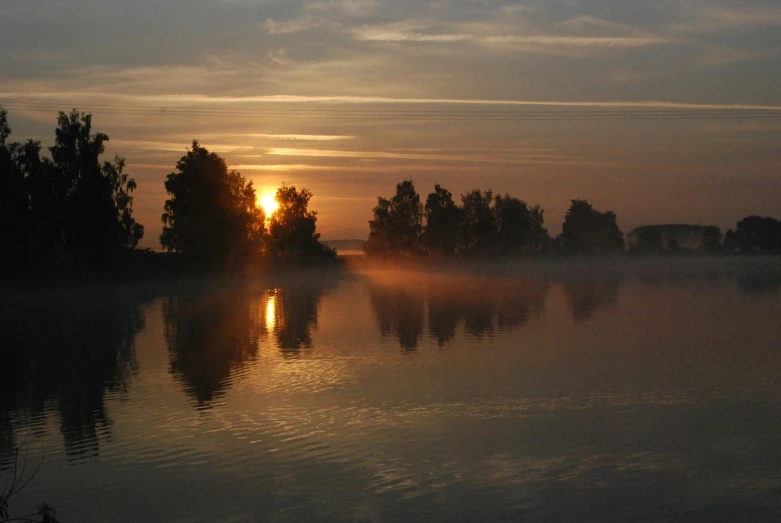 the sun is setting over a body of water, by Jan Tengnagel, pexels contest winner, romanticism, light orange mist, trees reflecting on the lake, great river, summer setting