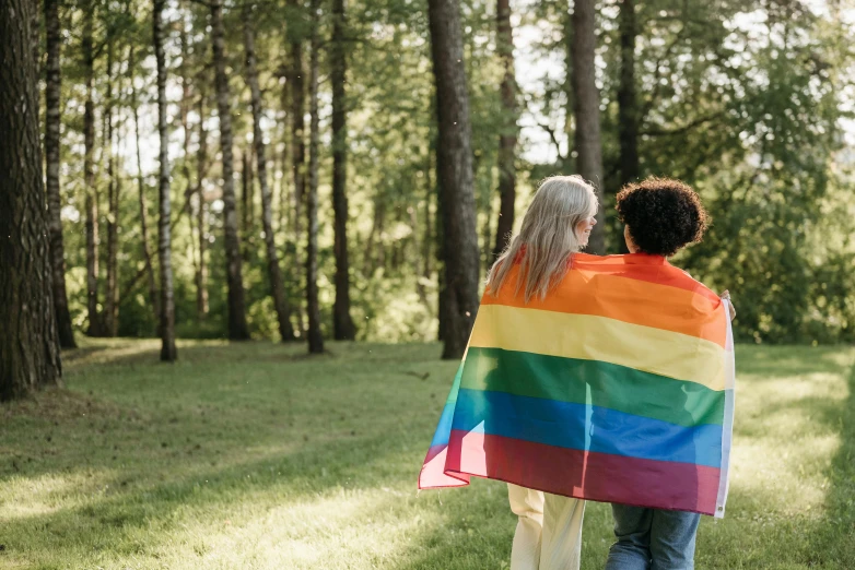 a couple of people that are standing in the grass, by Arabella Rankin, pexels, lgbt flag, forest picnic, a wooden, where a large