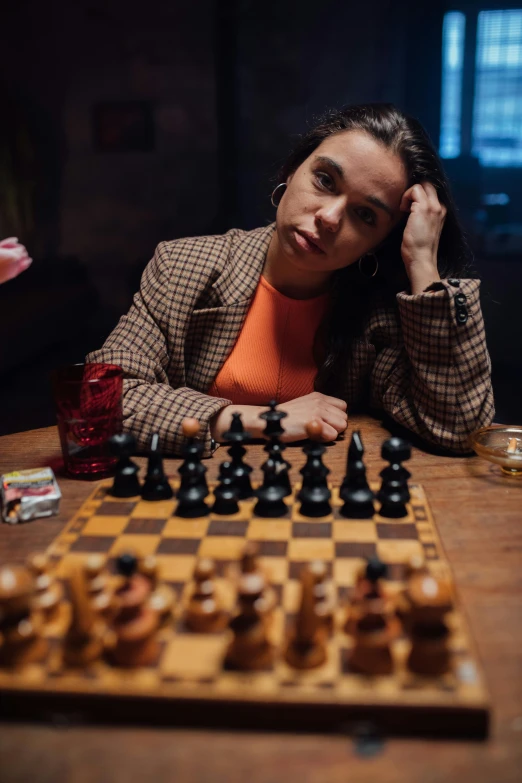 a woman sitting at a table with a chess board, a portrait, by Alejandro Obregón, pexels contest winner, wearing a turtleneck and jacket, thumbnail, hunting, **cinematic