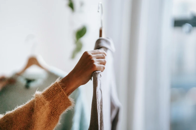 a woman hanging clothes on a hanger in a room, by Matija Jama, trending on pexels, wearing a grey robe, close up to a skinny, holding a wand, organic detail