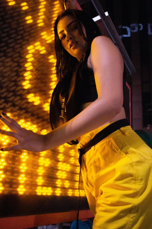 a woman in yellow pants and a black top, inspired by David LaChapelle, unsplash, visual art, model is wearing techtical vest, dua lipa, extreme backlighting, maisie williams