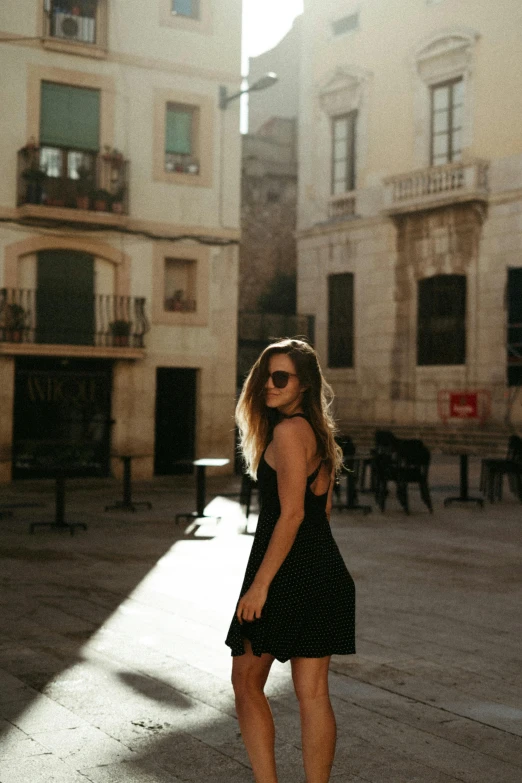 a woman in a black dress standing on a skateboard, by Modest Urgell, pexels contest winner, gothic quarter, sun glare, wearing a camisole and shorts, young woman in a dress