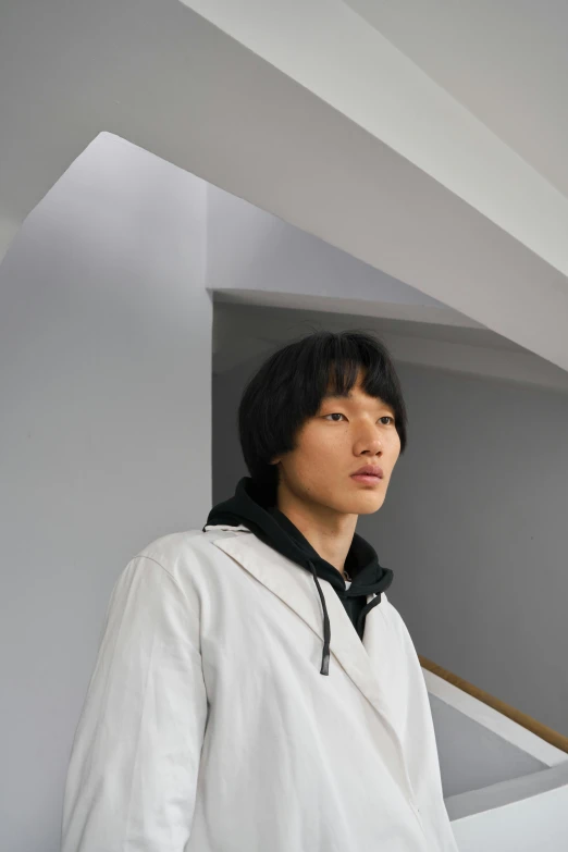 a man standing in front of a staircase, an album cover, inspired by jeonseok lee, unsplash, wearing a hoody, uniform off - white sky, model face, pengzhen zhang