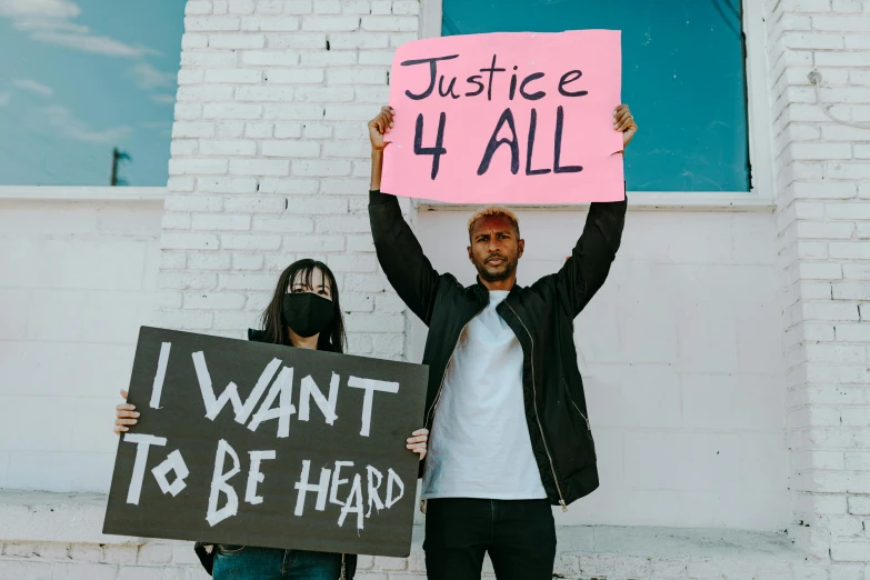 two people holding up signs in front of a building, by Julia Pishtar, trending on pexels, black arts movement, justice, a photo of a man, 3 4 5 3 1, anfree wallin