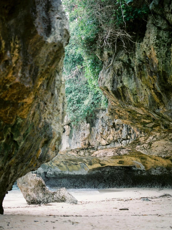 a couple of people standing on top of a sandy beach, natural cave wall, las pozas, 35mm print, lush nature