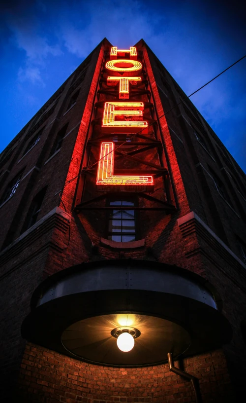 a neon hotel sign on the side of a building, by Dave Melvin, unsplash, multiple stories, historical photo, reddish exterior lighting, hello