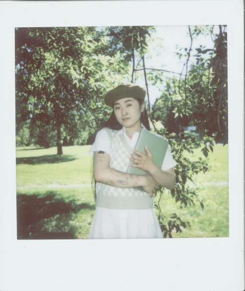 a woman in a hat holding a book, a polaroid photo, inspired by jeonseok lee, trees in the background, androgynous male, resembling a mix of grimes, scanned in