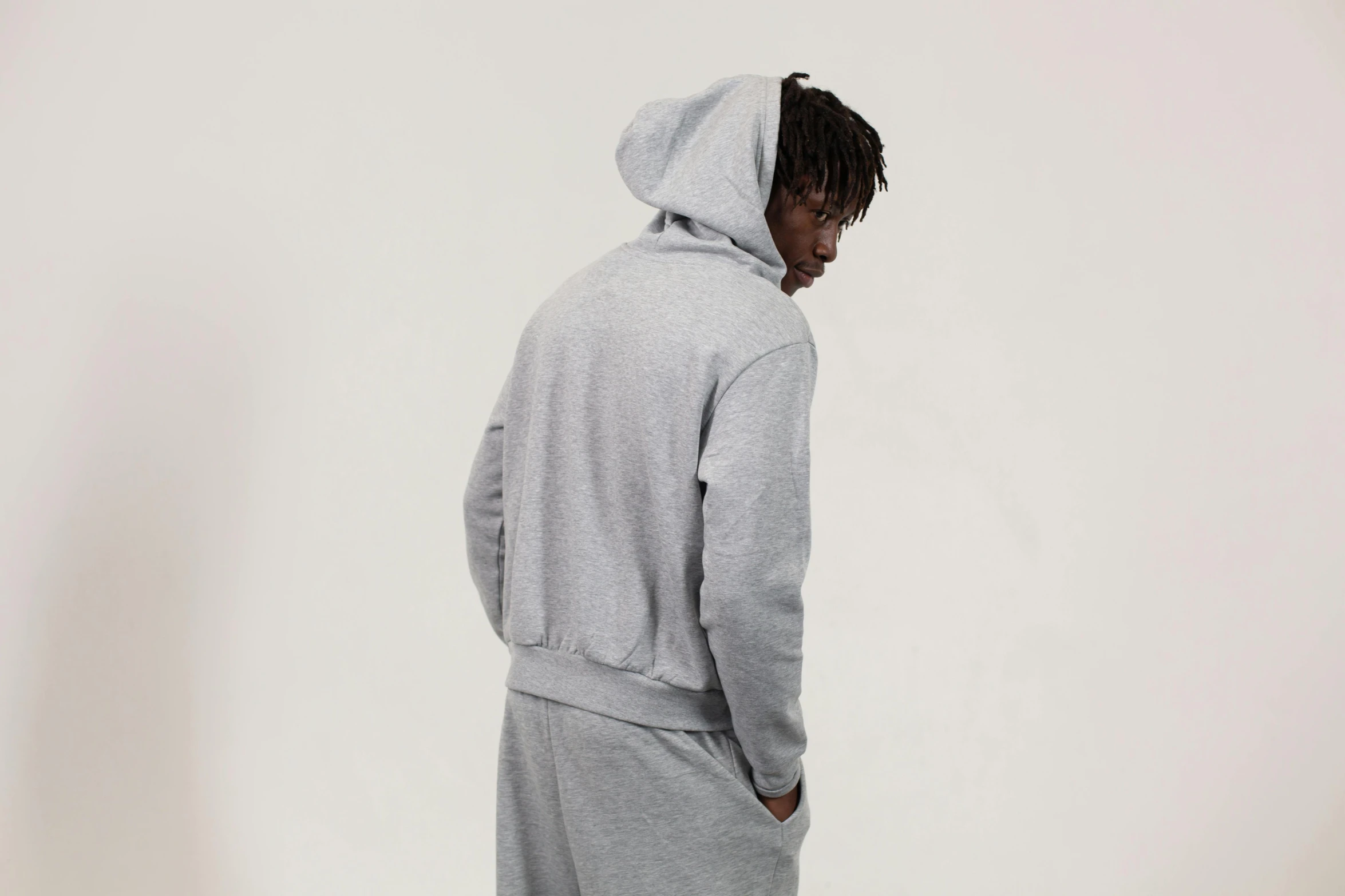 a man standing in front of a white wall wearing a grey hoodie, man sitting facing away, wearing a tracksuit, ignant, carefully crafted