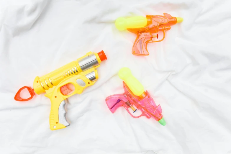 a couple of water guns laying on top of a bed, 3 heads, flatlay, shiny plastic, high quality product image”