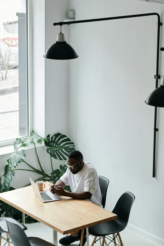 a man sitting at a table with a laptop, by Carey Morris, pexels contest winner, clean minimalist design, african canadian, greenery, low ceiling