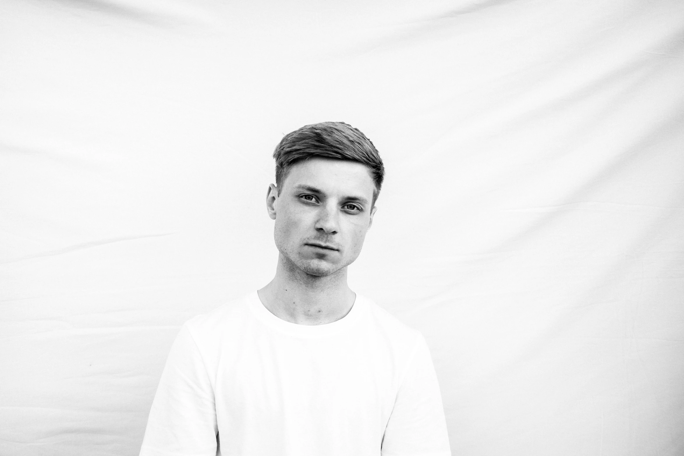 a black and white photo of a man holding a tennis racquet, a black and white photo, by Karl Buesgen, unsplash, lyco art, white wrinkled shirt, portrait of beautiful young man, dj, in front of white back drop