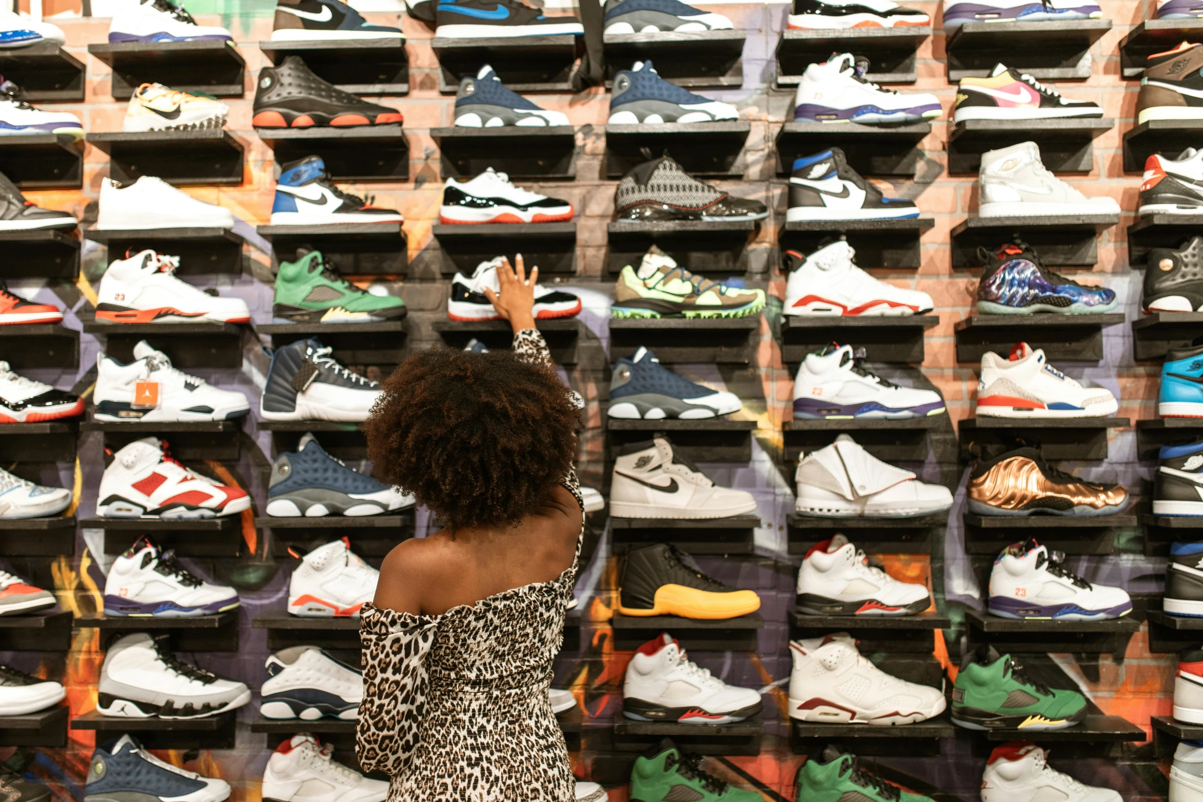 a woman standing in front of a wall of shoes, a cartoon, by John Platt, pexels, graffiti, virgil abloh, at a mall, “air jordan 1, birdseye view