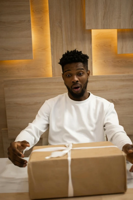 a man sitting at a table with a box in front of him, pexels contest winner, jaylen brown, giving gifts to people, all overly excited, professional modeling