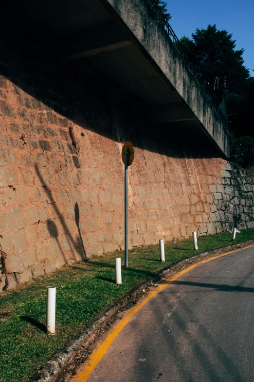 a man riding a skateboard down a curvy road, inspired by René Burri, street art, trees cast shadows on the wall, 1990s photograph, sao paulo, stone wall