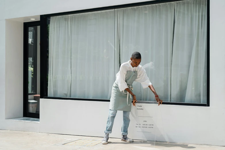 a man that is standing in front of a window, by Lily Delissa Joseph, temporary art, restaurant, woman holding sign, sweeping, in front of white back drop