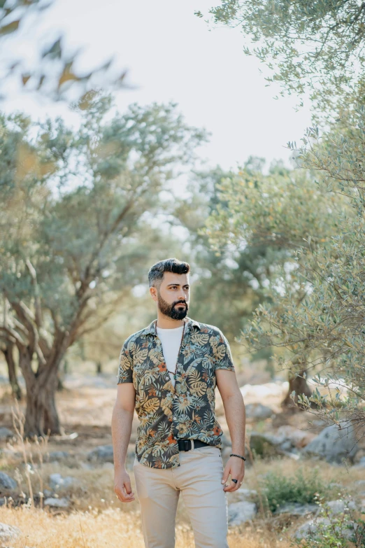 a man standing in the middle of a field, an album cover, inspired by Exekias, pexels contest winner, hurufiyya, elegant tropical prints, young greek man, casual clothing, wearing camo