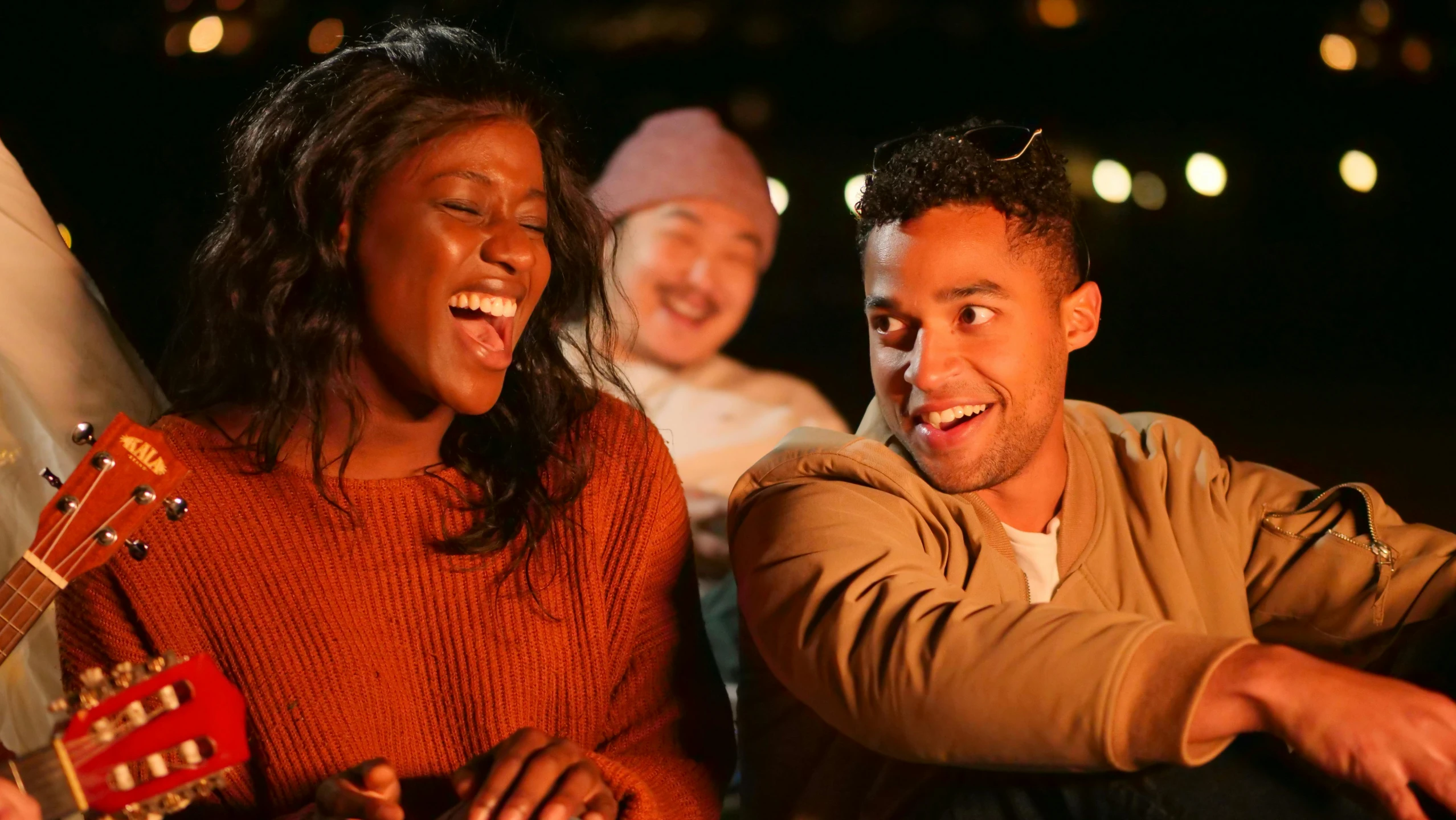 a man and a woman sitting next to each other with a guitar, trending on pexels, happening, brown skin man with a giant grin, night outside, holiday season, 3 actors on stage